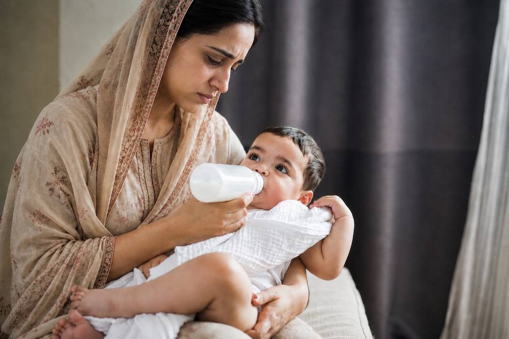 Tired mother holding feeder - Saara din ek haath mein feeder